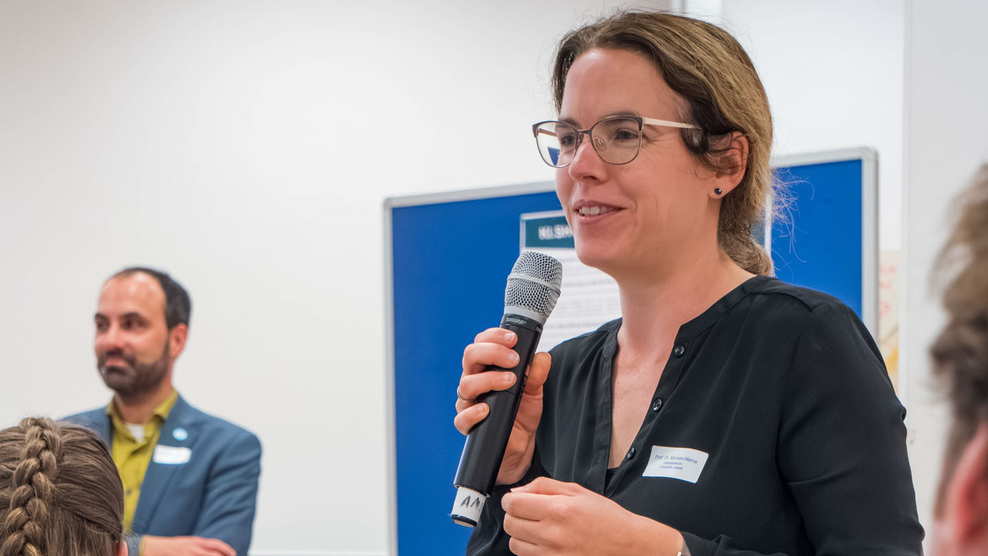 Eine Frau spricht vor einer blauen Pinnwand in ein Mikrofon